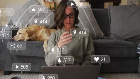 iconos digitales en burbujas de habla contra mujer caucásica usando computadora portátil mientras el perro duerme en el sofá