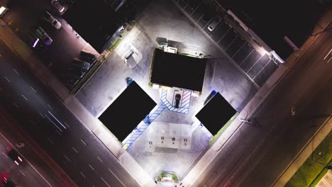 aerial drone time lapse top down view of a gas station at night at corner of intersection with cars driving with light streaks