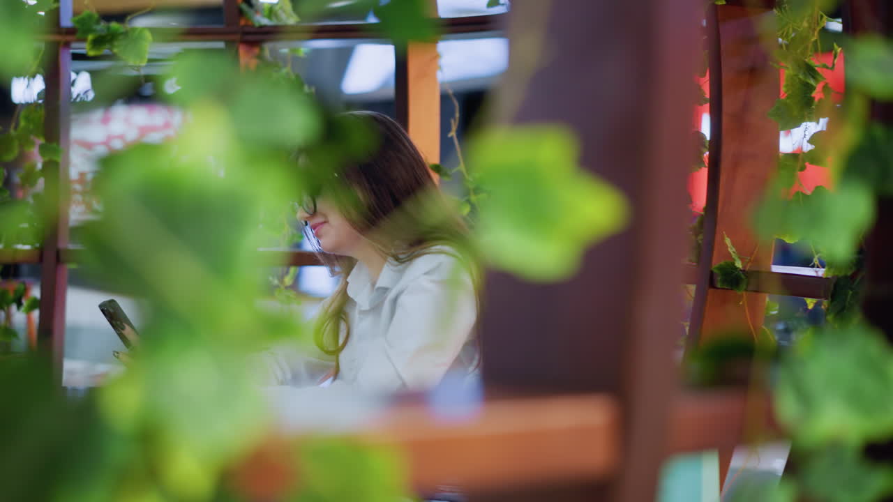 테이블에 앉아있는 행복한 젊은 여성, 전화로 약혼, 고양이 테마의 네온 조명 장식을 특징으로하는 편안한 배경으로 양쪽에 쇼핑 가방