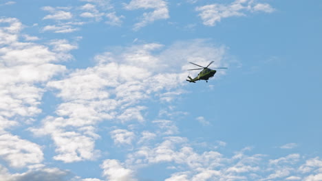 green ambulance helicopter approaching from a distance, against a blue sky