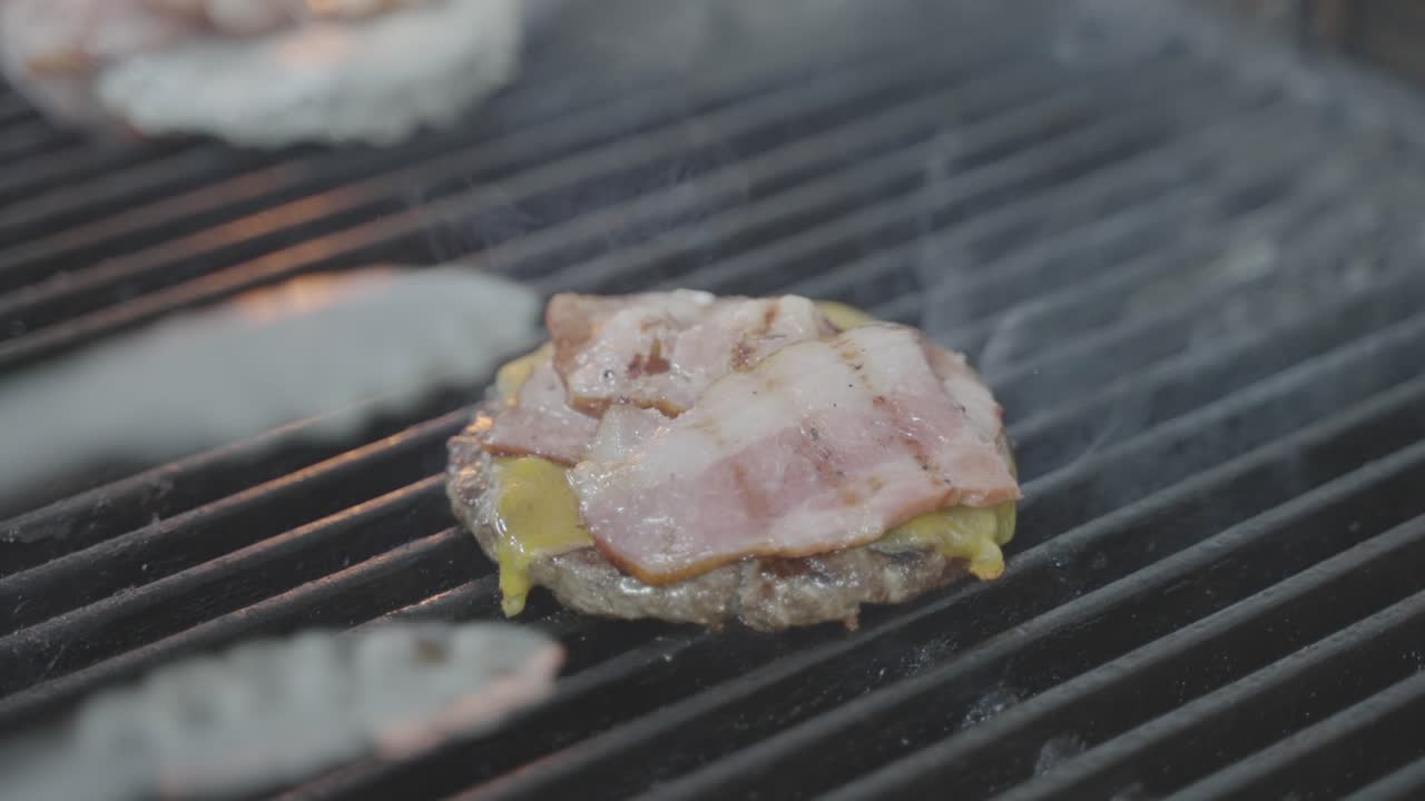 Chef putting bacon on burger meat grilling with cheese on grill