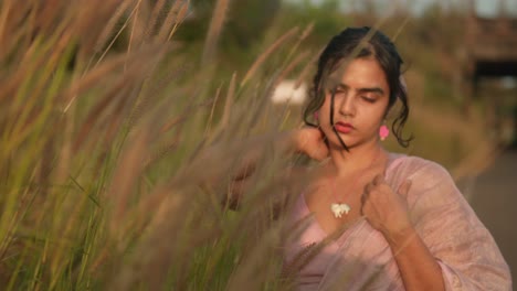 young woman in a field at sunset, touching tall grass, with warm light casting a glow on her face