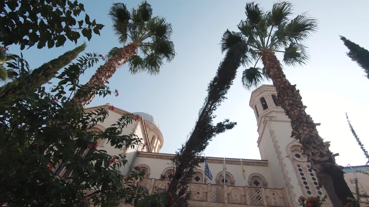 Tall exotic Palm Trees parallel to lateral aisle Agia Napa Cathedral Towers in Limassol, Cyprus - Wide low angle slow rotation shot