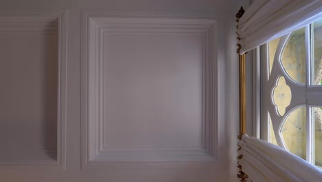 down up view of carved castle ceiling next to a big window with curtains