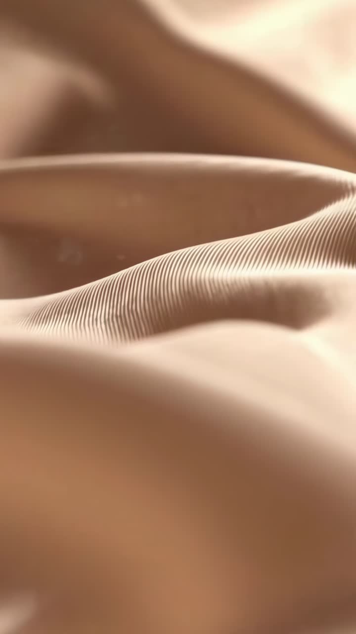 Video ravvicinato di un tessuto liscio e fluente con illuminazione soffusa e una delicata texture ondulata