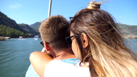 rear back view of young unrecognizable couple spending time together on deck of sailboat at sunny day. beautiful girl hugging her boyfriend from behind on boat during trip. vacation or holiday concept. close up