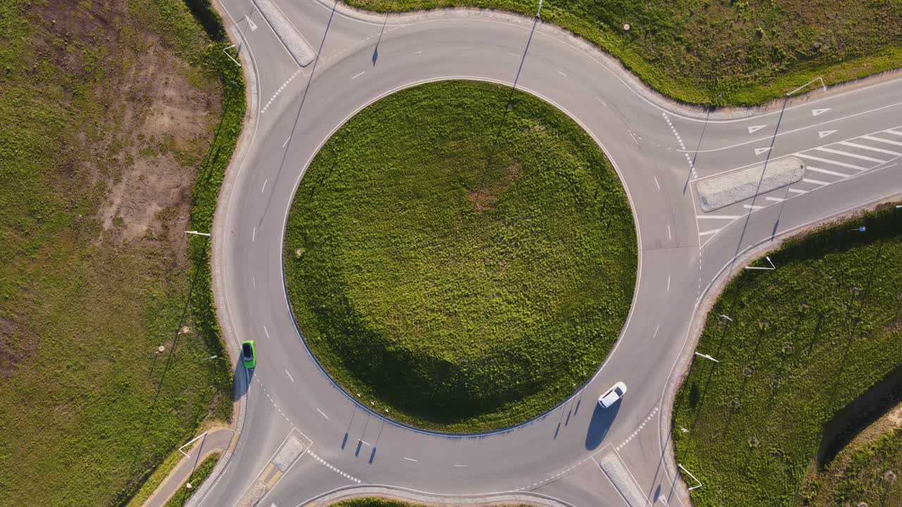 Traffic moves through green suburb around large circular road structure from above, top shot static