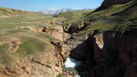 epic revealing cinematic drone shot of a small waterfall underneath an overpass near the kel-suu lake in kyrgyzstan