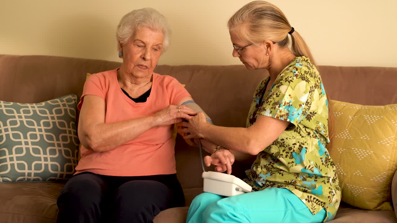Home healthcare nurse and elderly woman taking blood pressure with a machine