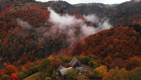 La-Inclinación-Aérea-Hacia-Arriba-Revela-Una-Casa-De-Campo-Cerca-Del-Valle-De-La-Montaña,-Un-Bosque-De-Colores-Otoñales.