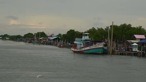 a touring thai boat on the right side of the estuarine ready to go out the the ocean, piers and boats are also revealed, a community of seamen and fishermen.