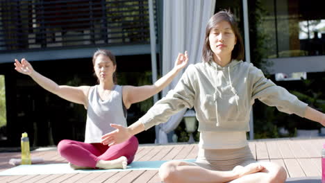 Fokussierte-Asiatische-Freundinnen-Praktizieren-Yoga-Meditation-Auf-Sonniger-Terrasse,-Zeitlupe