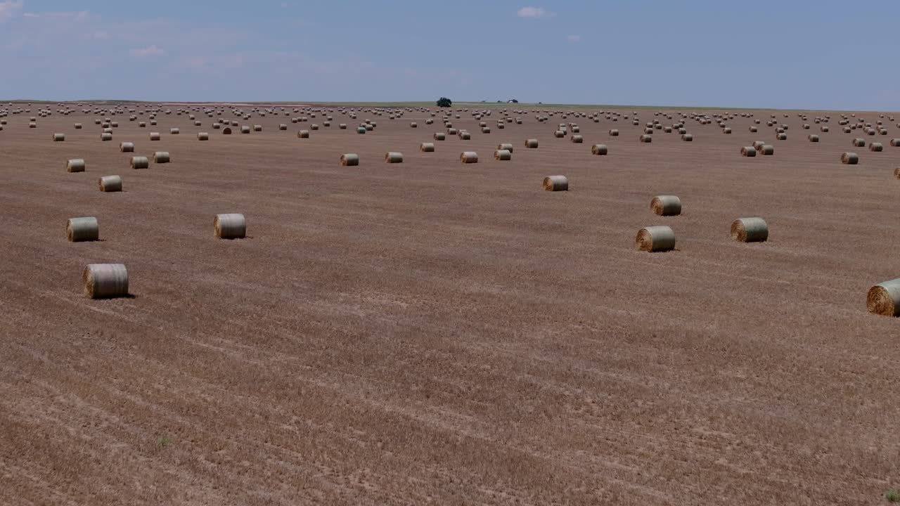 Aerial panoramic establishing repeating hay bale rows across vast Great Plains USA agricultural farmland field