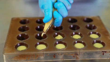 handmade manufacturing of chocolate. filling the molds with creamy stuffing from pastry bag. close up.