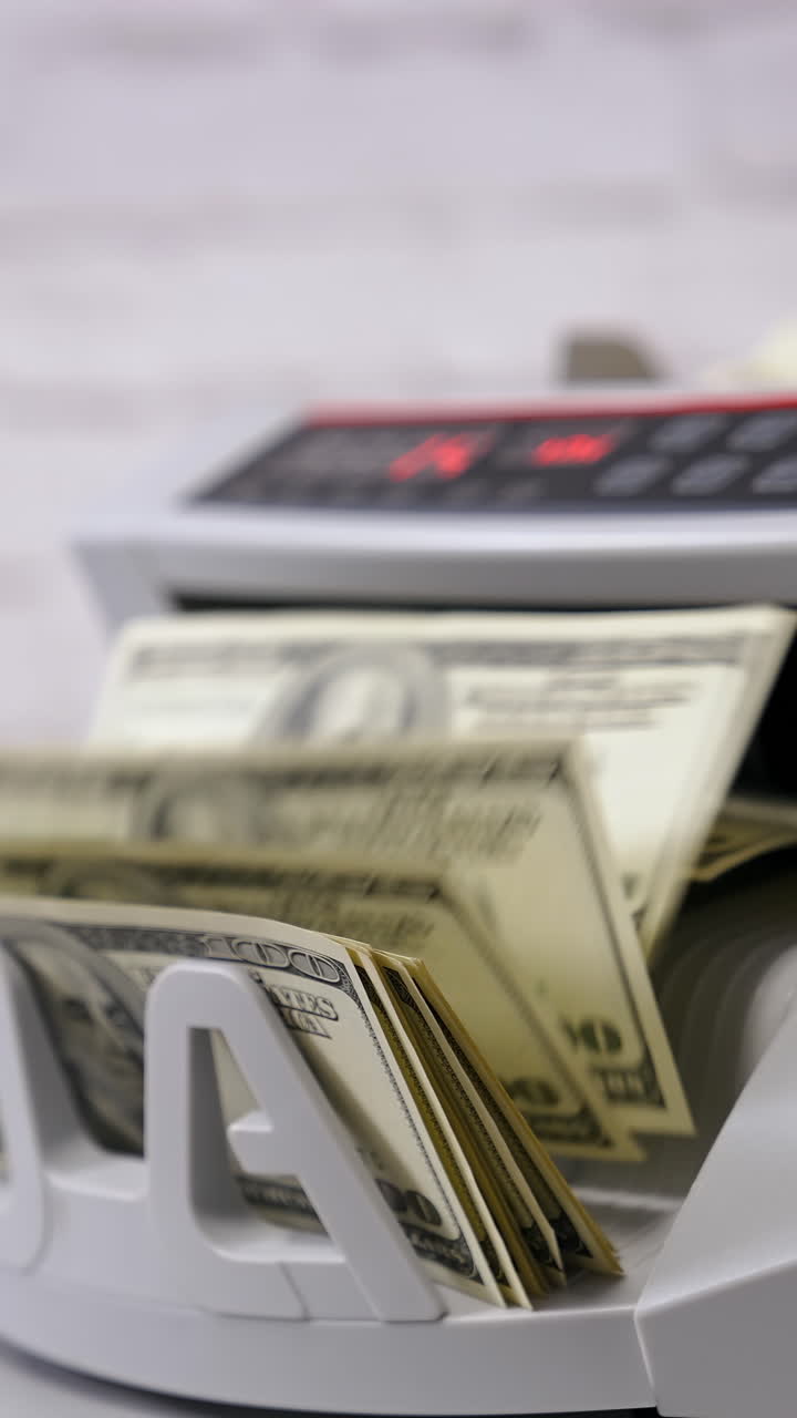 Bank automatic equipment for calculation paper currency. Currency counting machine counting dollar bills. Female worker taking out a bundle of one hundred usd from automatic machine. Side view. Vertical video