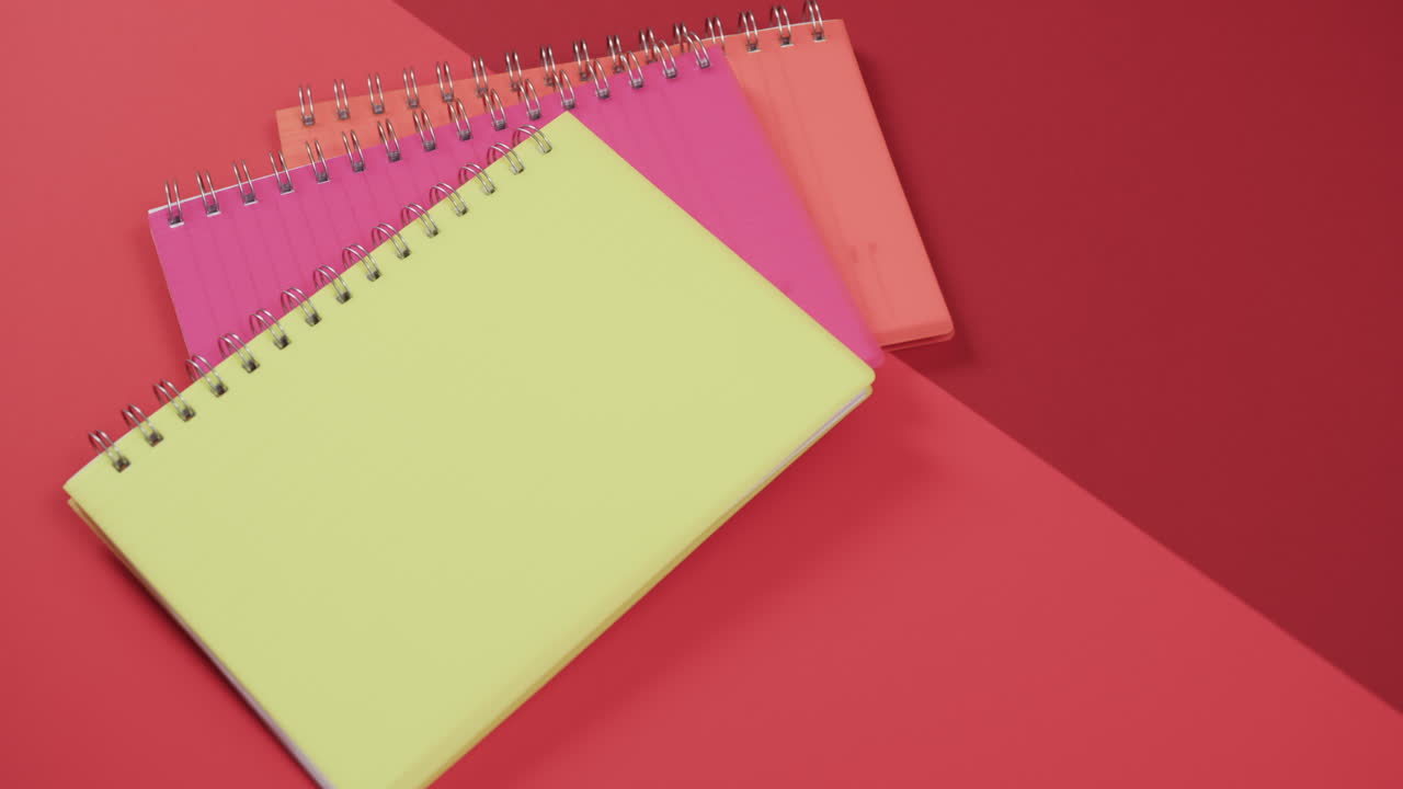 vista aérea de cuadernos coloridos sobre fondo rojo, en cámara lenta
