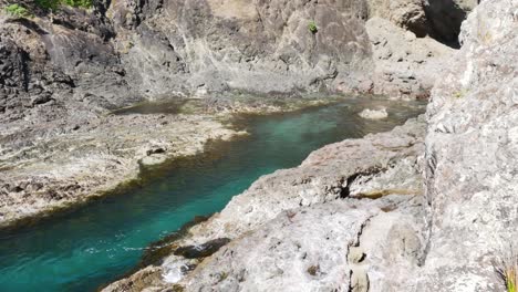 Crystal-clear-mountain-river-flowing-between-rocks-during-sunny-day---Spirits-Bay,New-Zealand---Panning-shot