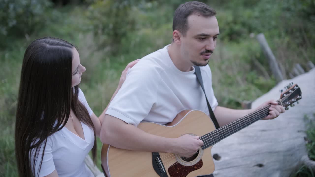 A man and a woman singing and playing guitar outdoors
