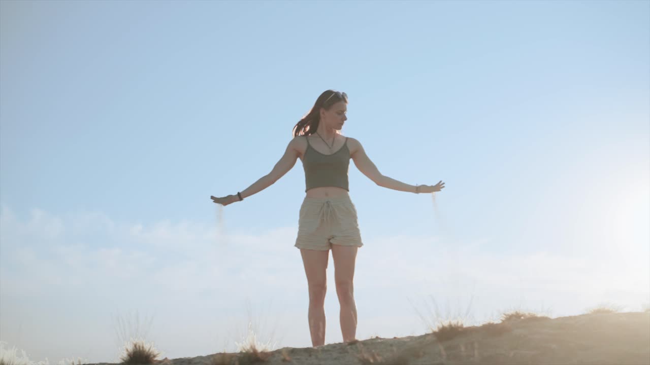 Young woman in desert letting sand slipping through hands, slow motion