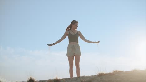 young woman in desert letting sand slipping through hands, slow motion