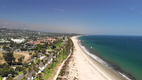 Drone-Aéreo-Disparó-Sobre-La-Playa-De-Arena-Y-El-Océano-Pacífico-Azul-Oscuro-Con-Cometas-En-Santa-Barbara,-California