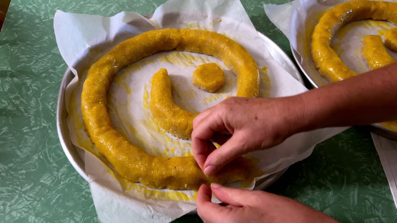 Close up of woman's hands decorating a traditional Italian cake, the Torciglione or tortiglione, with coffee beans for eyes and white candy in its mouth. For cooking, holiday, or cultural content