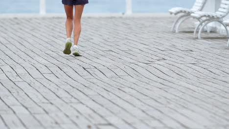 slow motion capture of woman jogging on brick-paved road, lower half, legs