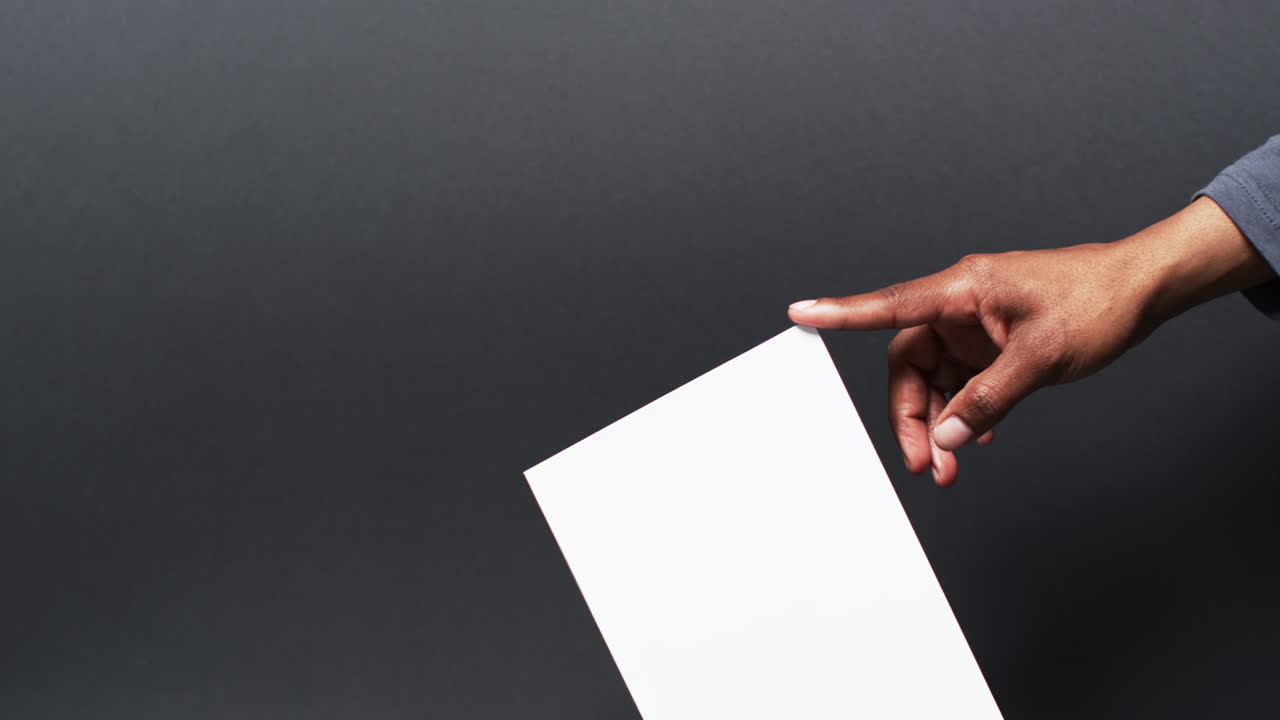 Video of hand of african american man holding book with blank pages, copy space on black background