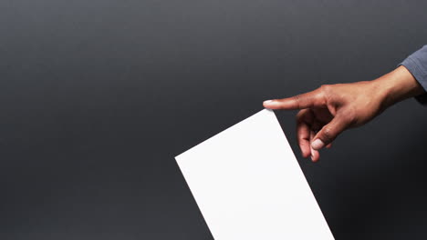 Video-of-hand-of-african-american-man-holding-book-with-blank-pages,-copy-space-on-black-background