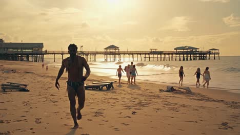 man walks on sandy beach at sunset with pier in background