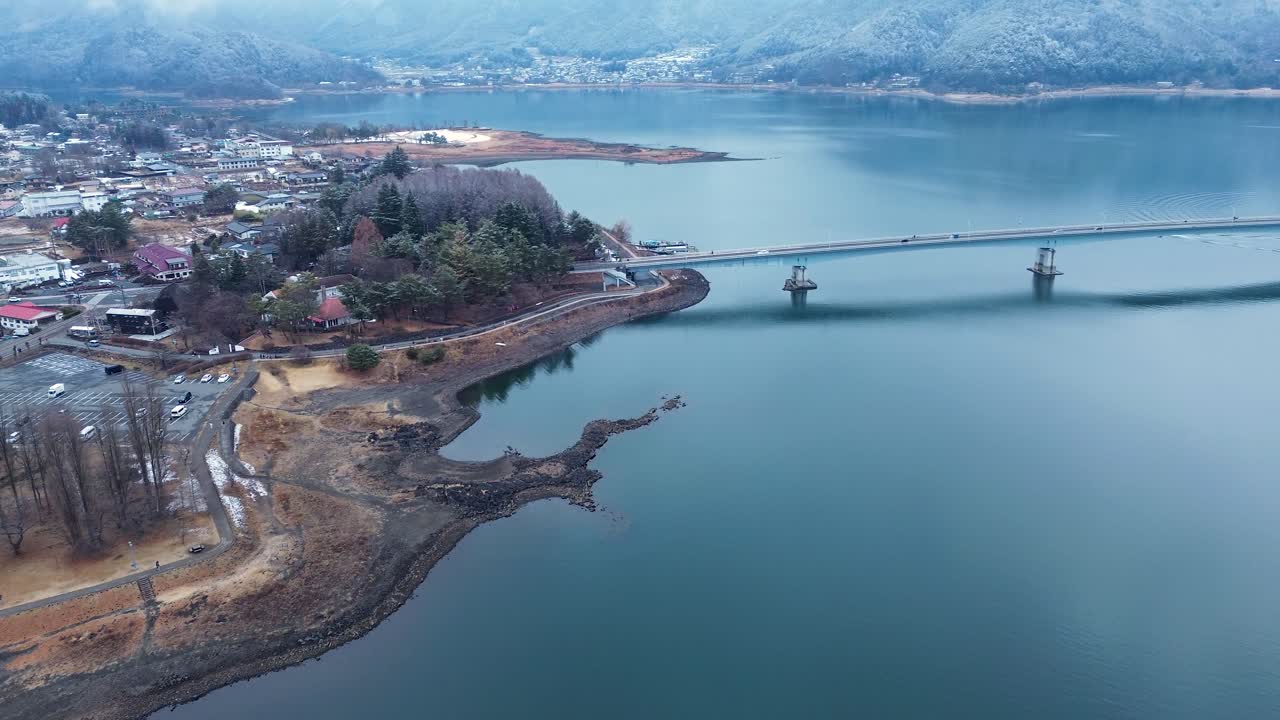 Paesaggio aereo con drone di veicoli che viaggiano lungo l'autostrada del ponte Kawaguchiko-ohashi sull'insenatura del lago, con un promontorio montuoso nebbioso e fitti alberi della foresta, nella zona turistica del Monte Fuji, Yamanashi, Giappone.
