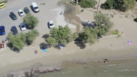 calm waves hitting the sandy shoreline of beach with cars parked on the parking lot in summer