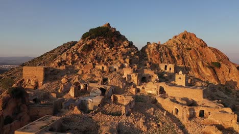 una lenta toma de un dron en círculos de un antiguo pueblo en túnez durante una cálida puesta de sol golpeando la ladera rocosa a su lado