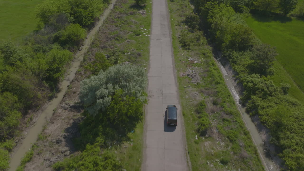 Veduta con drone di un'auto nera che percorre una strada rurale.