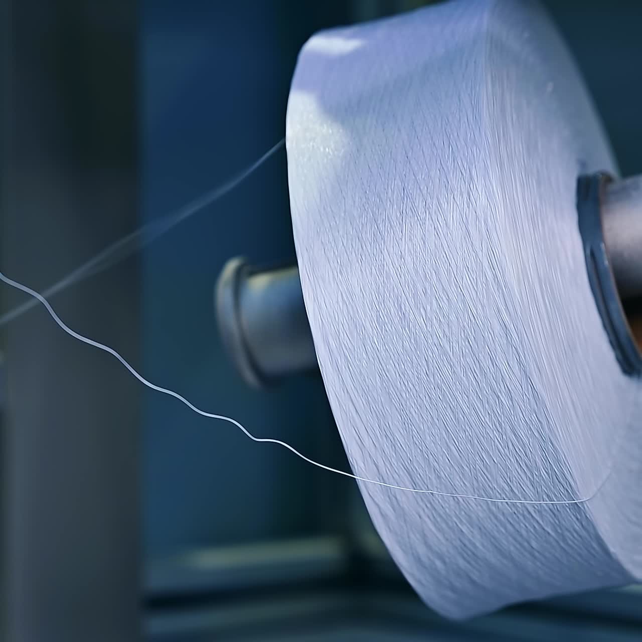 Two big reels of white yarn at the diaper manufacture. Unwinding a bobbin of white thread. Close up