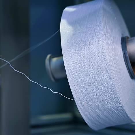 two big reels of white yarn at the diaper manufacture. unwinding a bobbin of white thread. close up