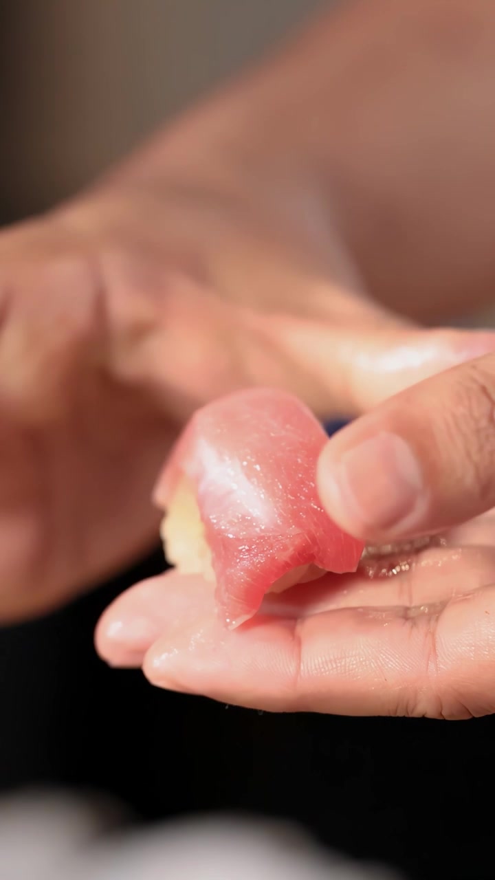 Close up shot of a chef's hands skillfully shaping raw tuna over seasoned rice