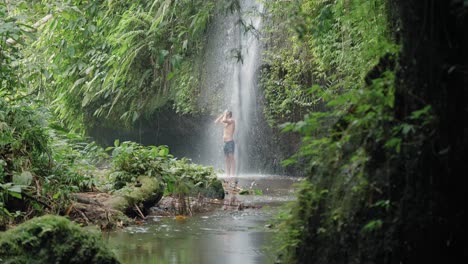 attractive man showering underneath waterfall and cooling off on summer day