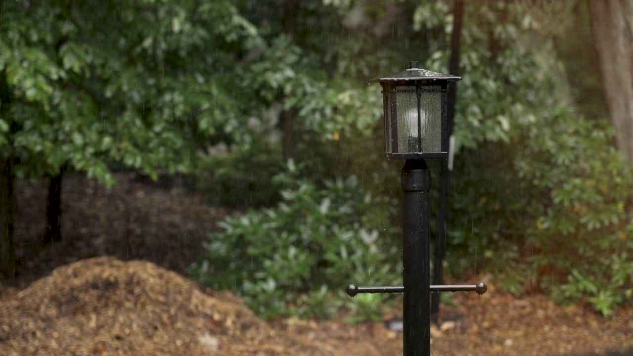 Slow motion look at huge rain drops falling on a lamp post.