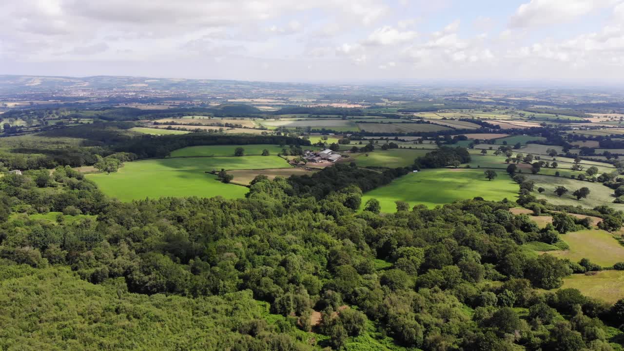 Aerial perspective showcasing expansive lush greenery, forested areas, and open fields within a picturesque countryside setting, capturing the charm of rural landscapes under a clear blue sky.
