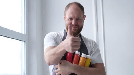 handsome young bearded artist stands and holds tubes of paints