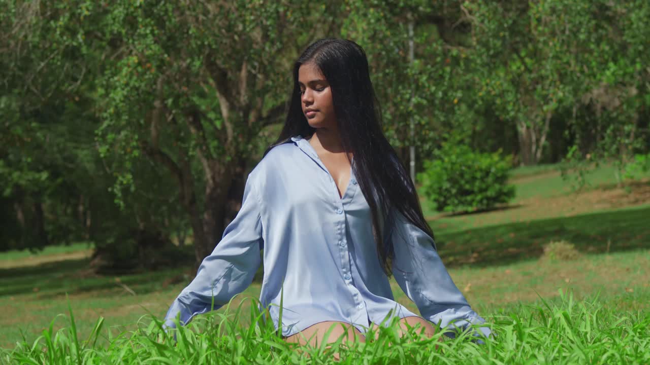 con una camisa azul, una joven india oriental en un parque arrodillado en la hierba