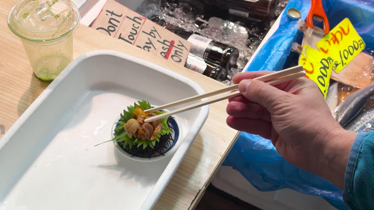 Close-up shot of a hand using chopsticks to eat fresh uni at a market