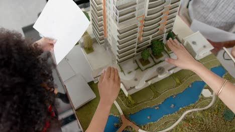 vista aérea de un equipo de diversos arquitectos discutiendo sobre un modelo de edificio 3d en la oficina