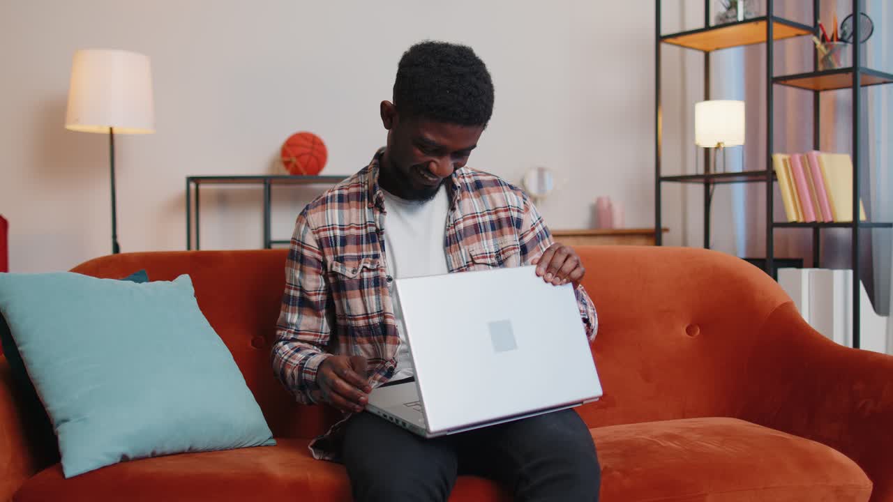 African american young man sitting on sofa closing laptop pc after work online in living home room