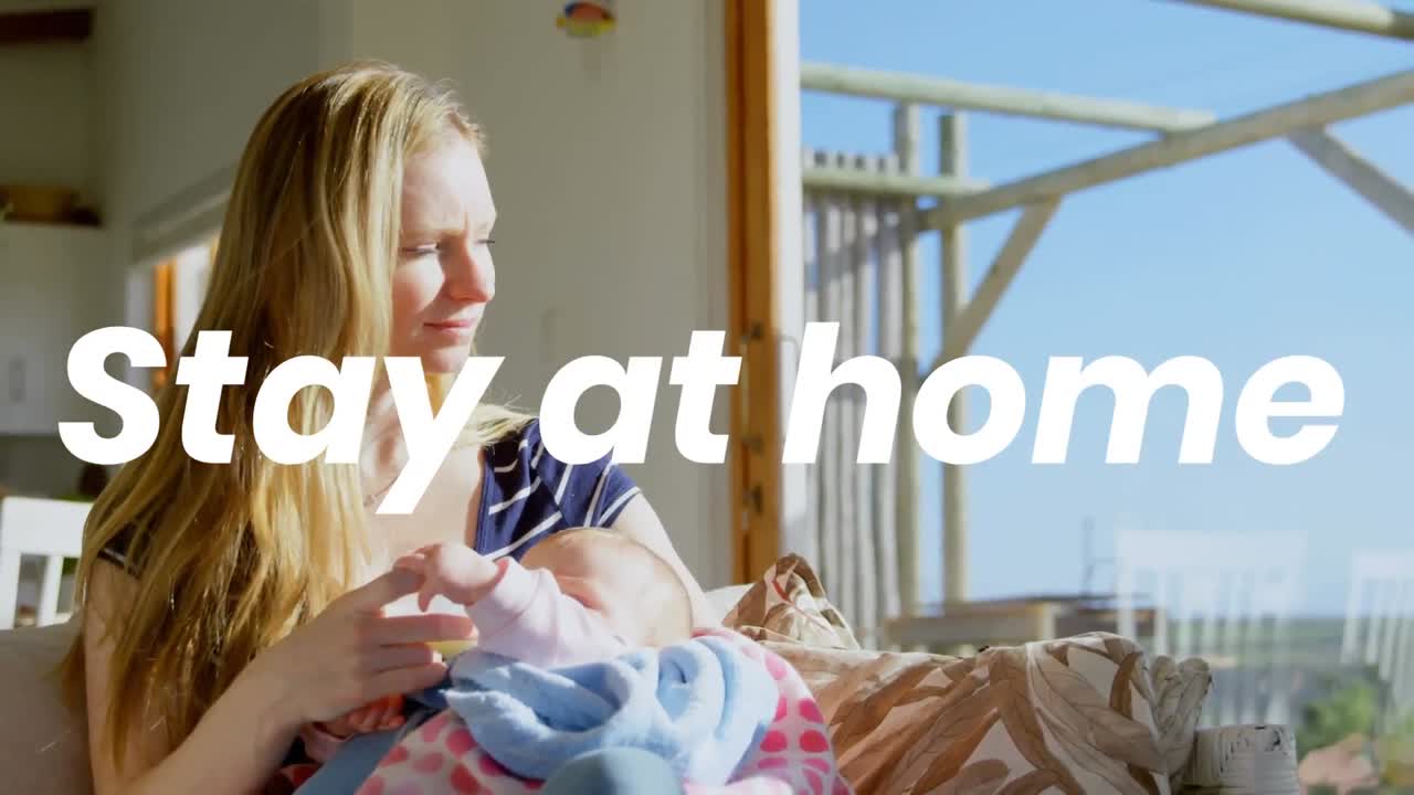 Kaukasisk kvinde og hendes baby derhjemme under coronaviruspandemien med ordene 'Bliv hjemme'.