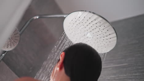 lady takes pleasant shower in apartment. modern big shower head produces streams of water to fall down on naked woman. woman washes in shower with tiled walls