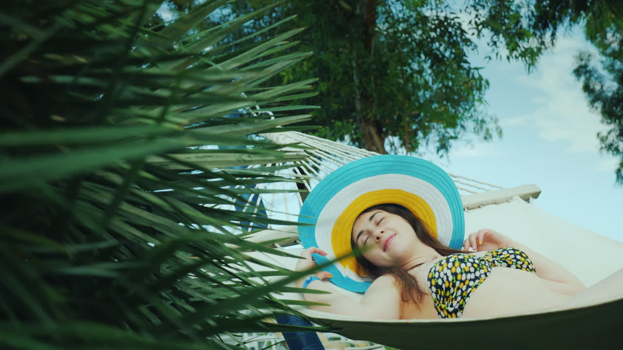 una linda joven sonríe soñadoramente yace en una hamaca de playa rodeada de palmeras verdes