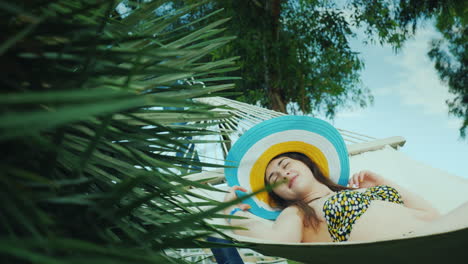 A-Cute-Young-Woman-Dreamily-Smiles-Lies-On-A-Beach-Hammock-Surrounded-By-Green-Palms