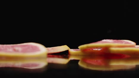 cámara lenta. anillos de pomelo en rodajas que caen con salpicaduras de agua en el vidrio sobre un fondo oscuro. cortado en rodazas.
